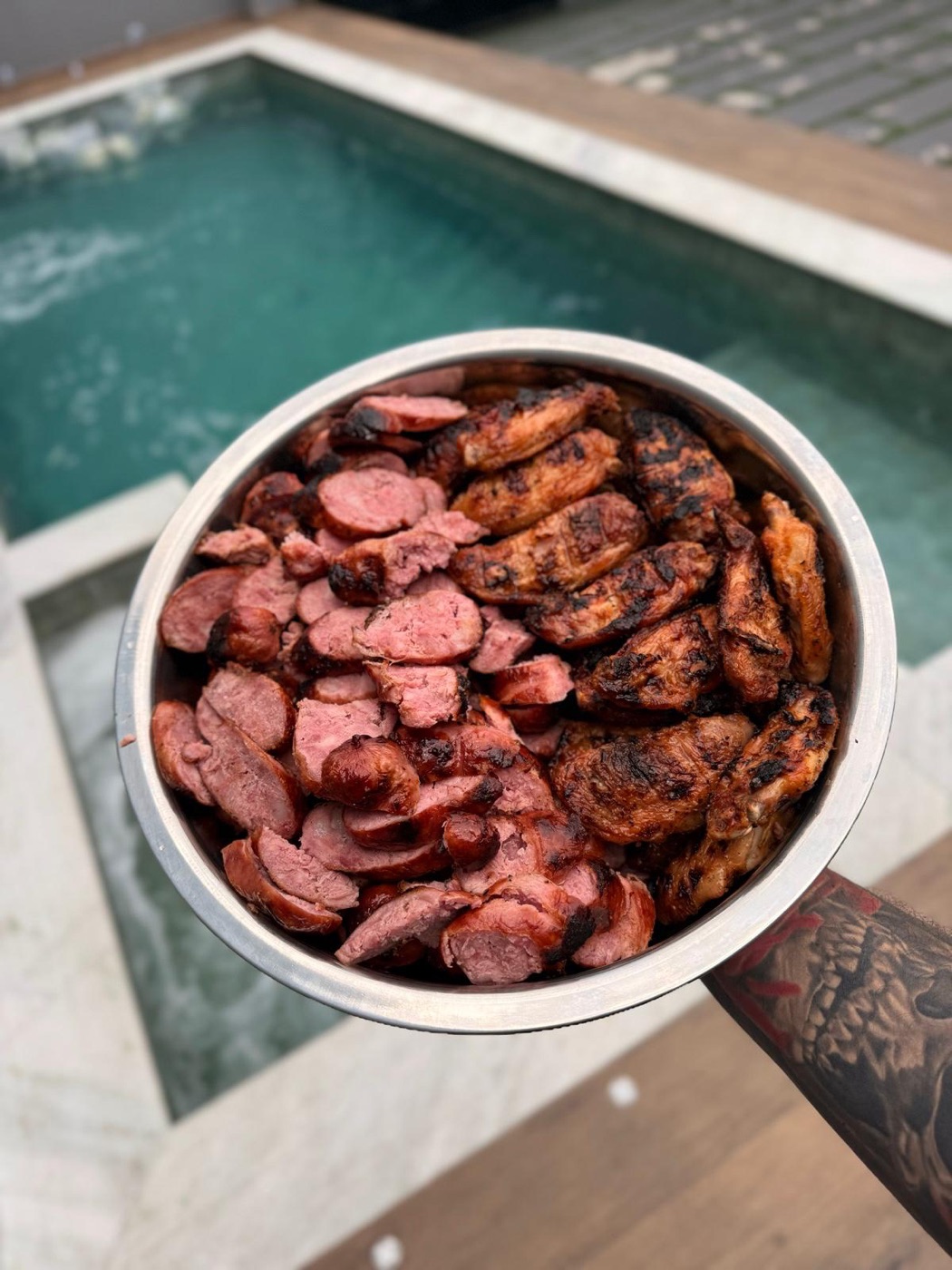 Bacia de linguiça e frango grelhados servida na beira da piscina